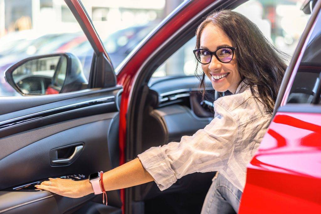 Good looking car saleswoman sitting in a new car and looking at the camera.