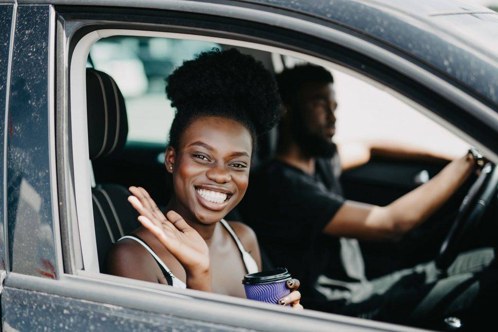 Smiling couple in car with coffee. girl looking at camera. man at the wheel. side view