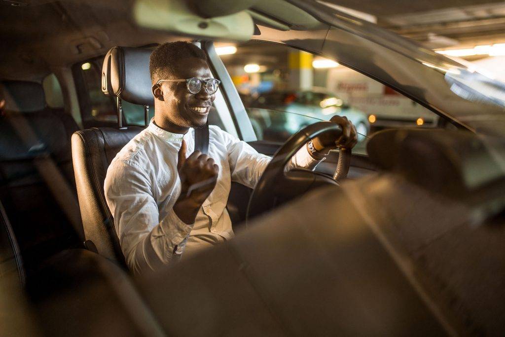 Happy African American businessman listening to music while driving his car.